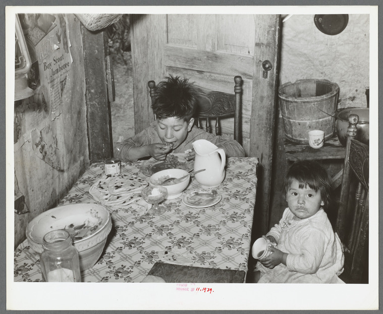 Two children eating at a kitchen table in an archival black-and-white photograph.